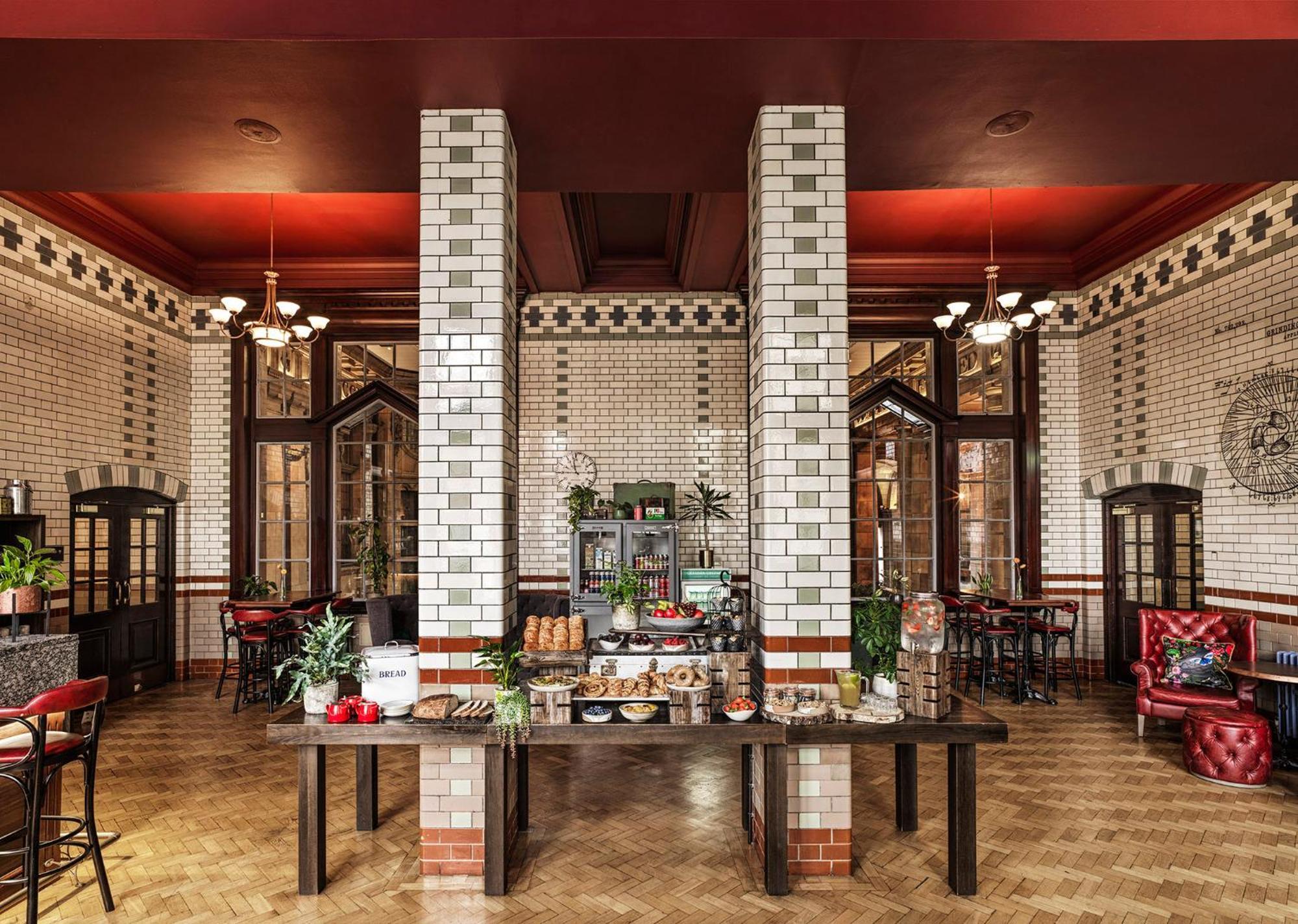 Kimpton Clocktower By Ihg Otel Manchester Dış mekan fotoğraf The photo shows an elegantly designed interior of a restaurant or cafe. The space features tall white tiled walls with decorative tiles, a high ceiling with red accents, and intricate moldings. In the center, there is a large wooden table displaying 