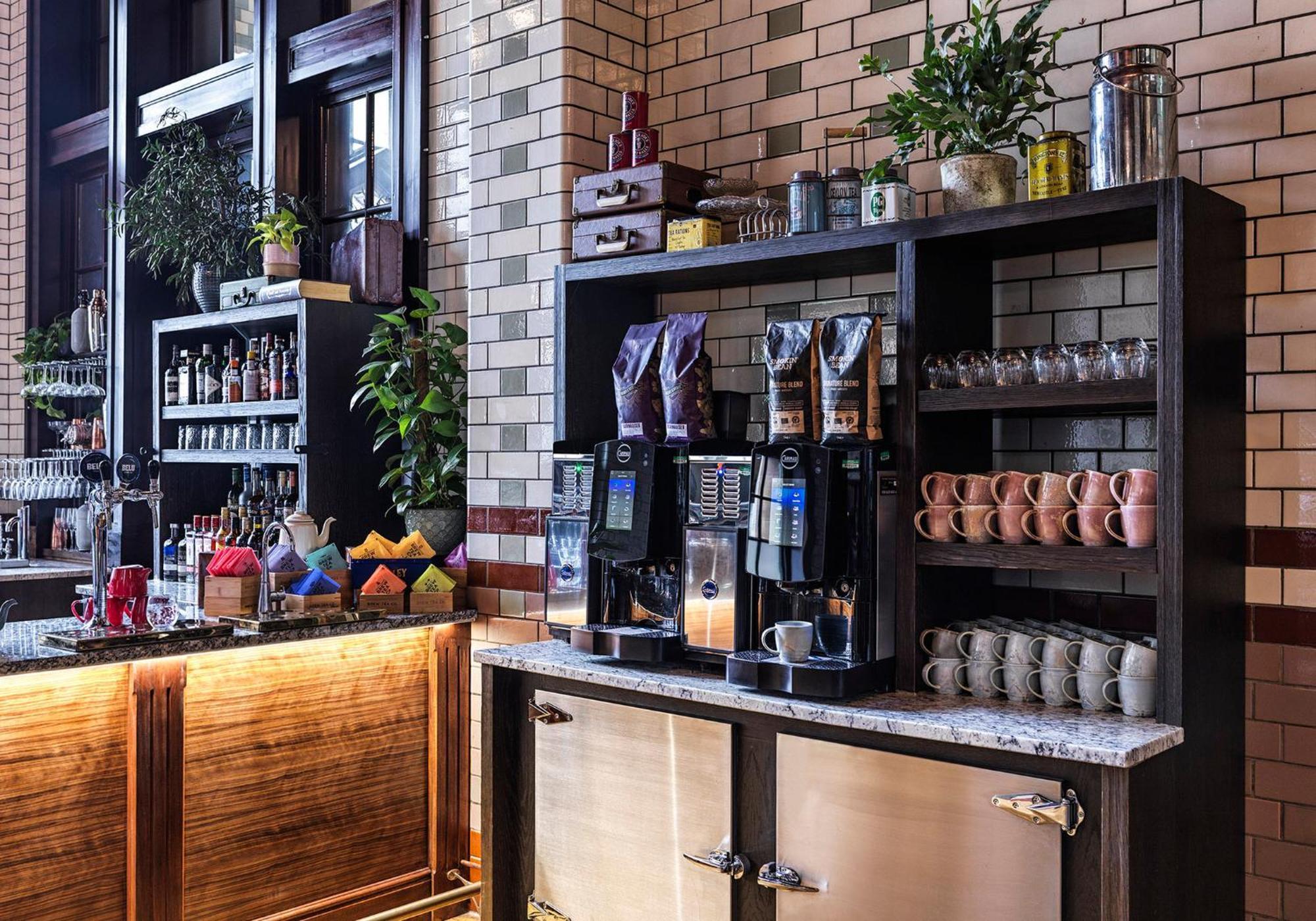 Kimpton Clocktower By Ihg Otel Manchester Dış mekan fotoğraf The photo shows a coffee station in a stylish café or restaurant setting. There are two coffee machines on a countertop, with coffee bean containers placed above them. The backdrop features a brick wall, giving it a modern yet rustic feel. There are 